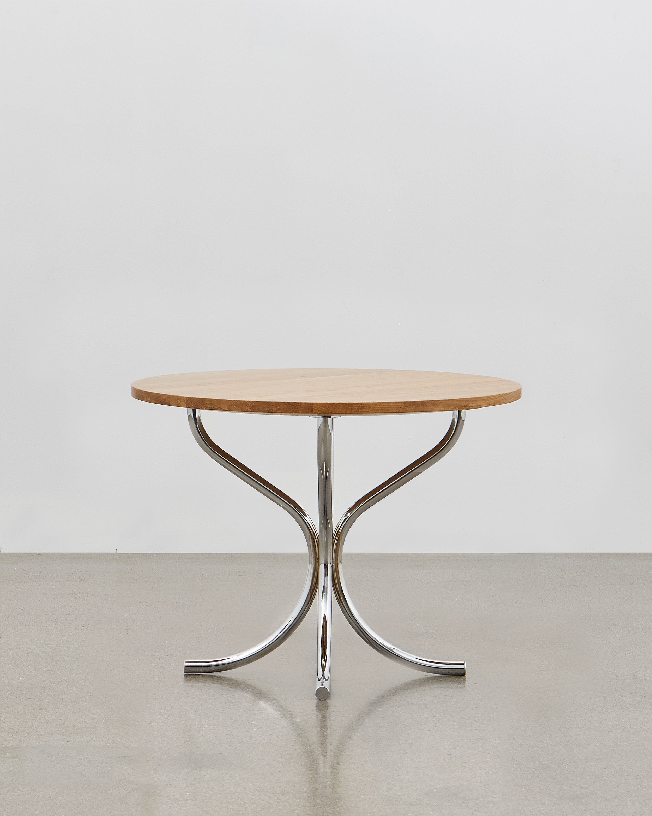 A round wooden lounge table with chrome metal legs, designed by Poul Henningsen.