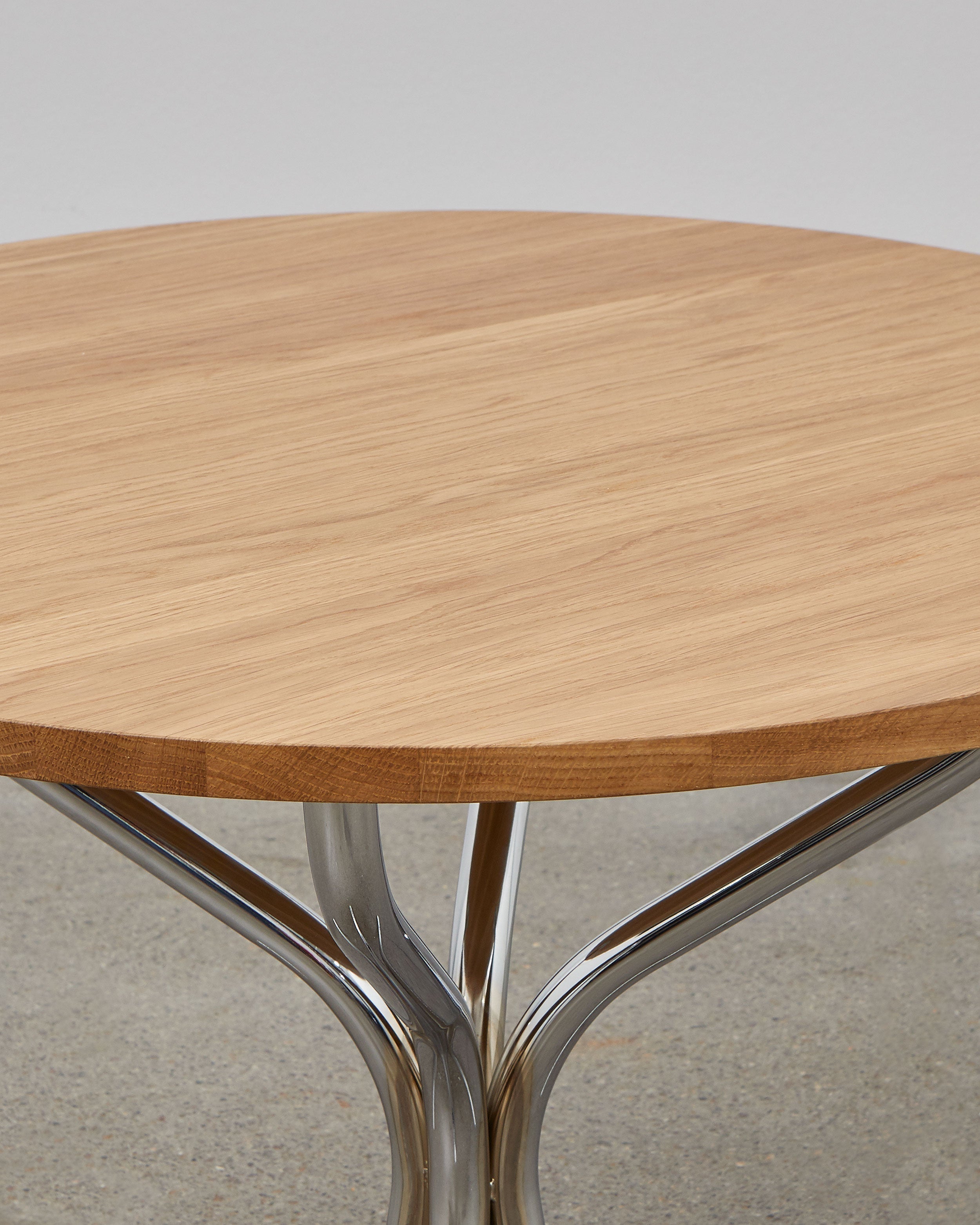 A round wooden lounge table with chrome metal legs, designed by Poul Henningsen.