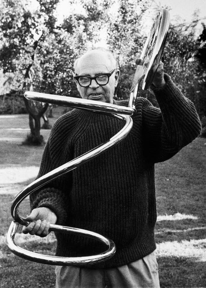 Poul Henningsen holding a modernist chrome chair outdoors with trees in the background. The chair is called PH Snake Chair