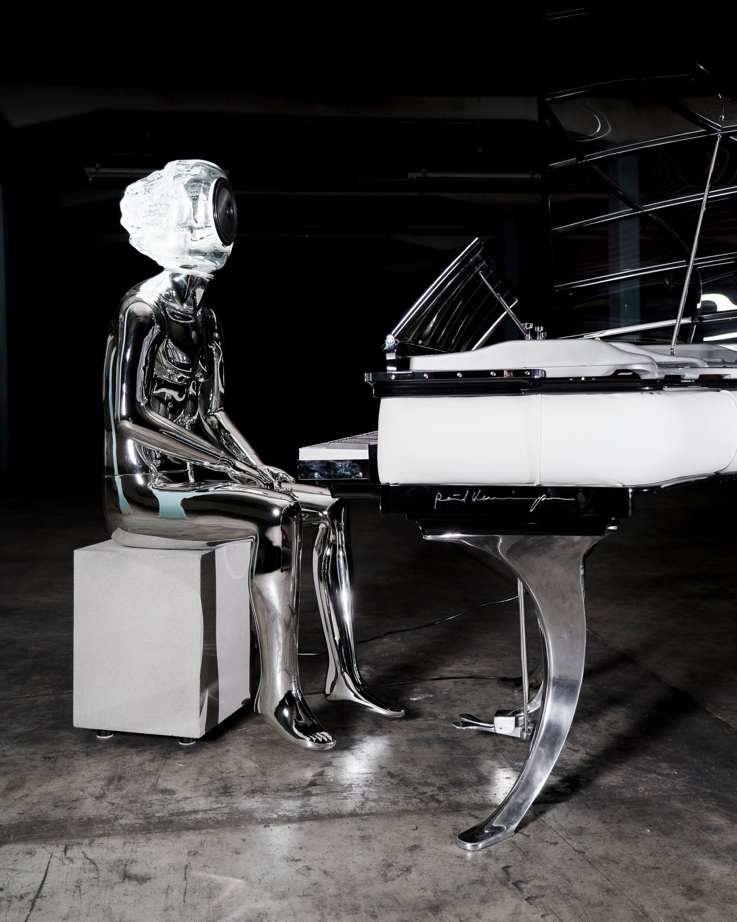 Audiomus is a audio design a chrome metallic sculpture of a seated figure on a concrete base with build in subwoofer and a mouth-blown glass sphere with light and the speaker driver built in 
