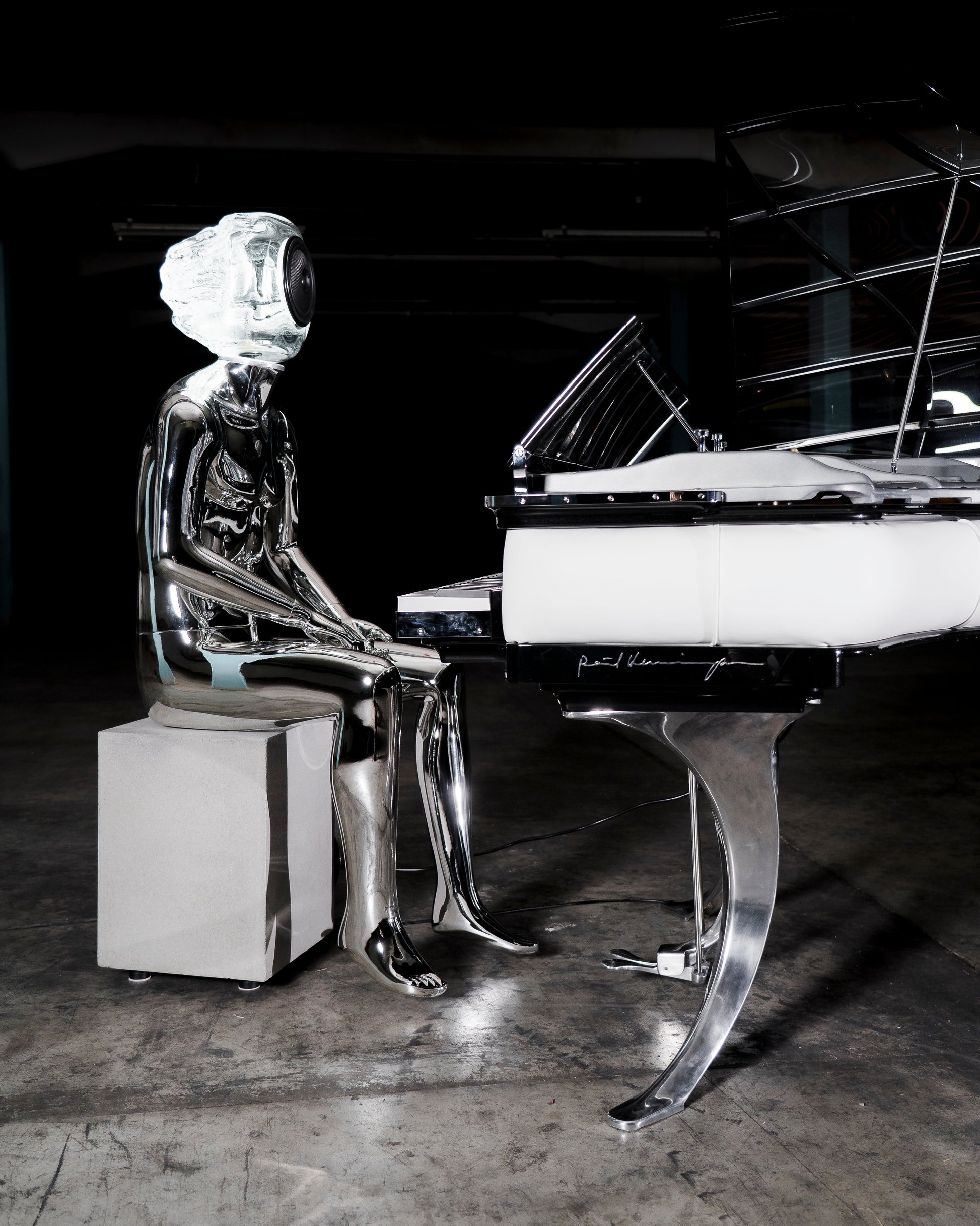 Audiomus is a audio design a chrome metallic sculpture of a seated figure on a concrete base with build in subwoofer and a mouth-blown glass sphere with light and the speaker driver built in 
