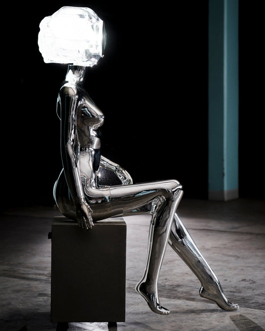 Audiomus is a audio design a chrome metallic sculpture of a seated figure on a concrete base with build in subwoofer and a mouth-blown glass sphere with light and the speaker driver built in 

