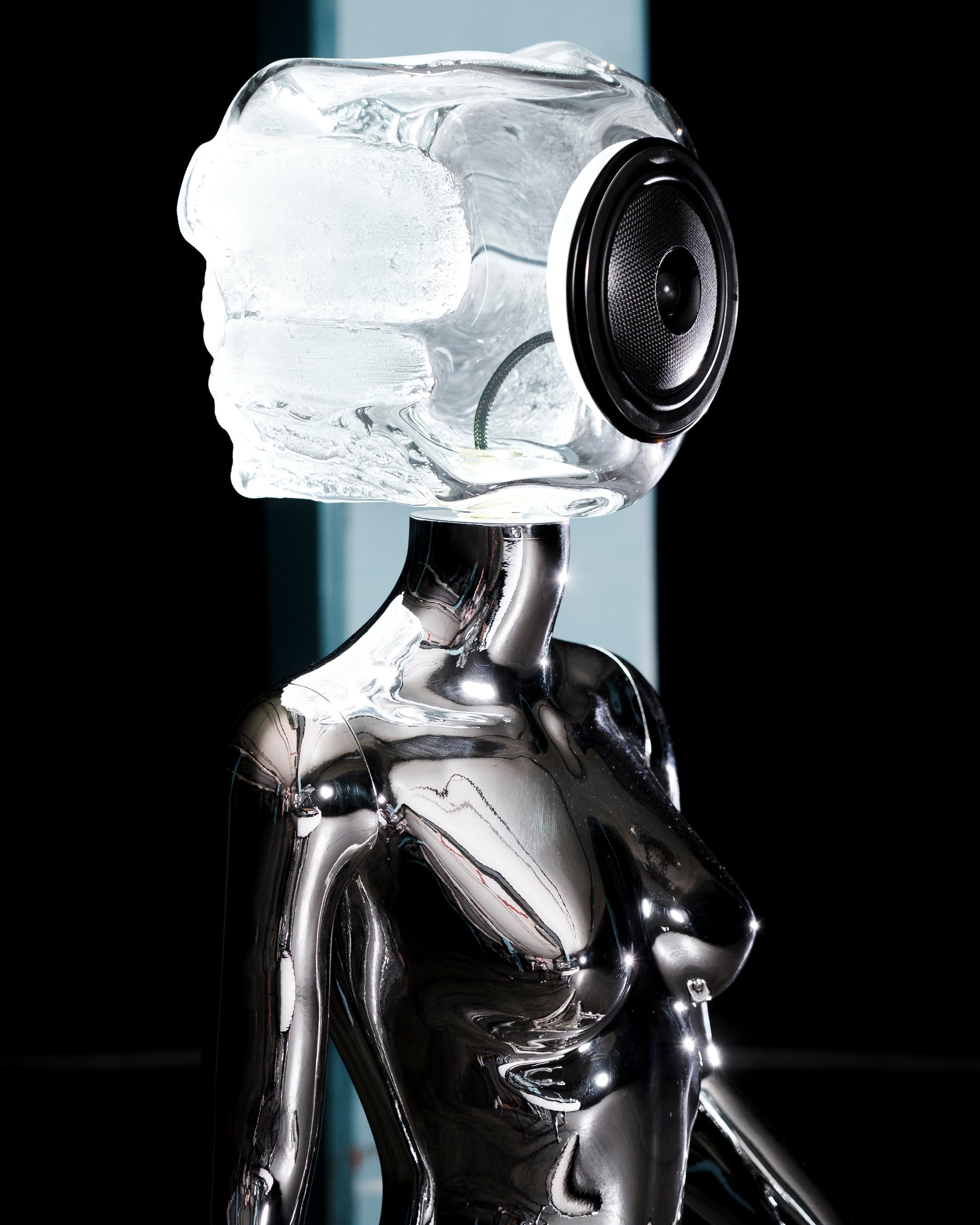 Audiomus is a audio design a chrome metallic sculpture of a seated figure on a concrete base with build in subwoofer and a mouth-blown glass sphere with light and the speaker driver built in 
