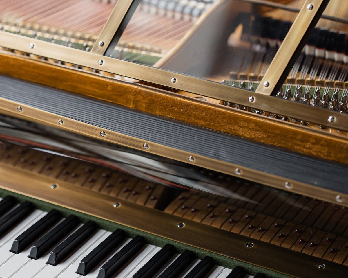 Close-up of a wooden grand piano showing the inner strings, metal framework, and part of the black-and-white keyboard.