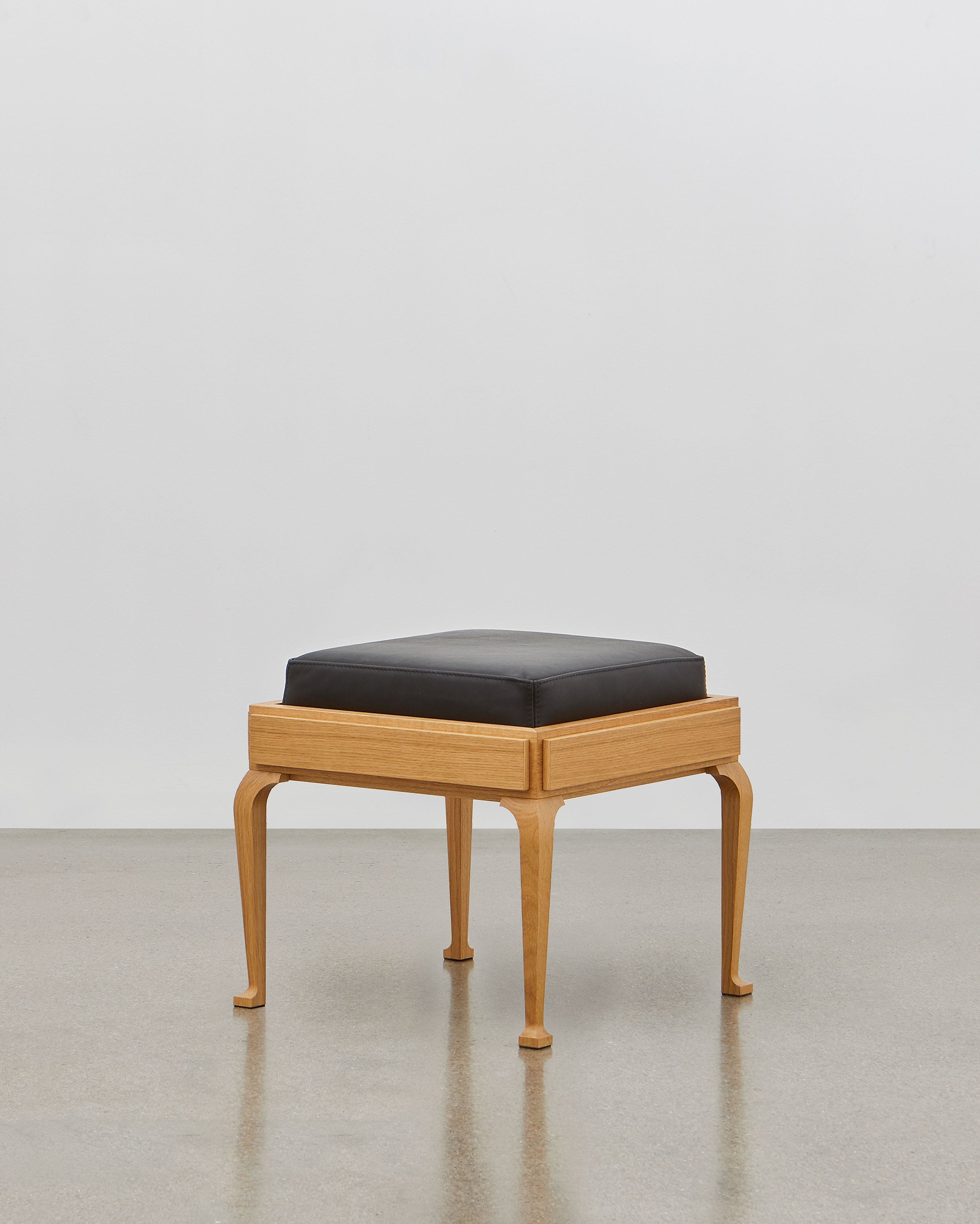 PH Stool by Poul Henningsen, Danish design classic (1920) A black upholstered stool standing on four angled wooden legs.
